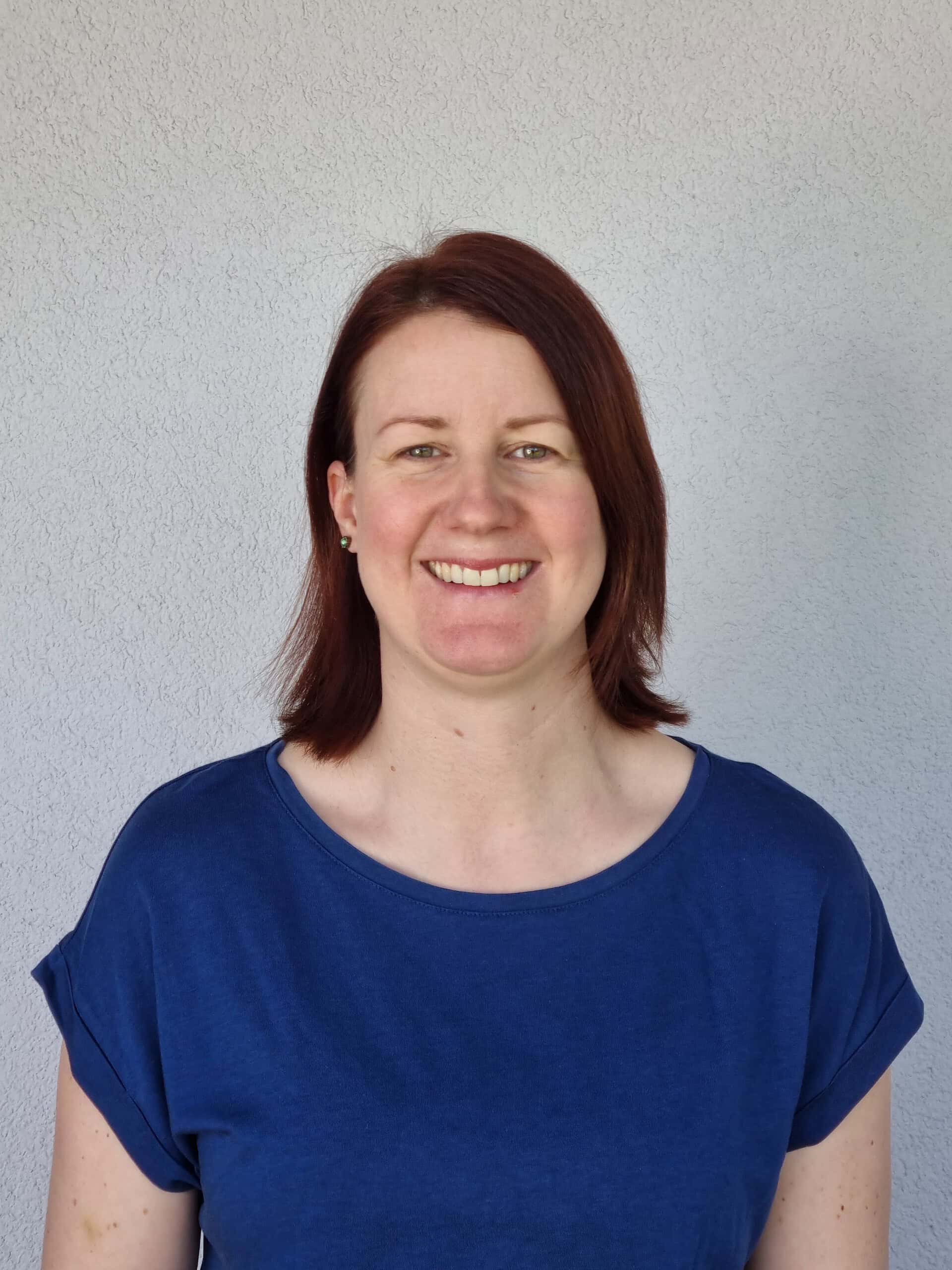 Lächelnde Frau in blauer Bluse vor neutralem Hintergrund.
